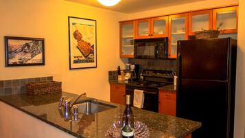 A kitchen with granite countertops, stainless steel appliances, wooden cabinets, and a framed poster on the wall.