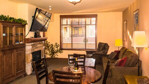 Un coin repas comprenant une table ronde, des chaises, un ventilateur de plafond, une cheminée et une fenêtre avec des stores.