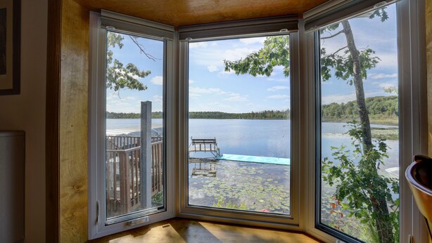 A corner room with large windows overlooking a lake, a wooden deck, and a bench.
