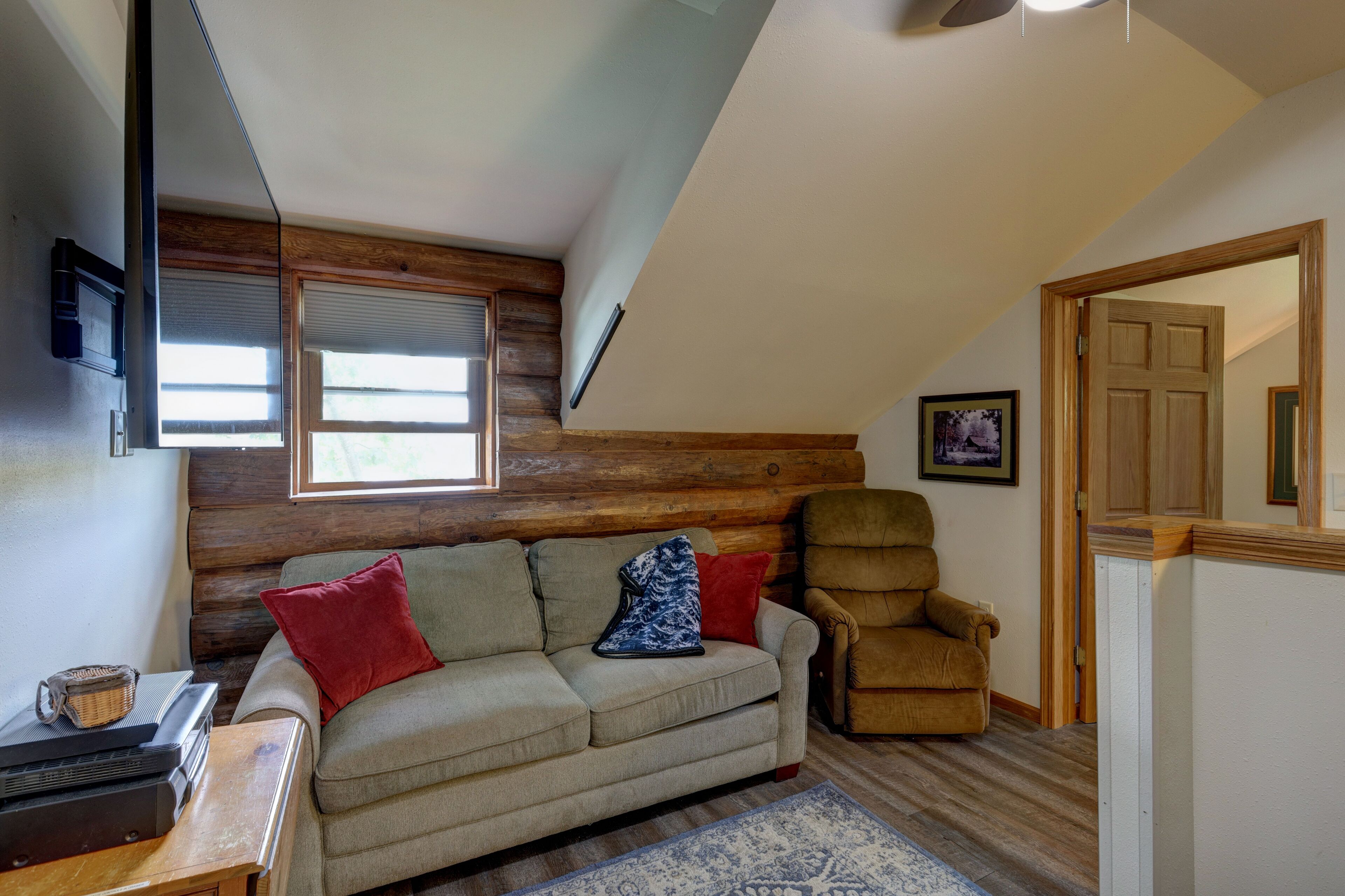 A cozy living room with a sofa, a chair, a wooden wall, and a door.