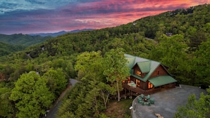 A cabin with a green roof, surrounded by dense forest, and a clear sky. - Curated, One of a kind 7,000 sqft. Lodge, VIEWS & Pool (Sevierville)