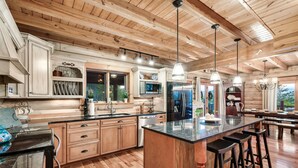 A spacious kitchen with wooden cabinetry, a large island with bar stools, stainless steel appliances, and pendant lighting. - Curated, One of a kind 7,000 sqft. Lodge, VIEWS & Pool (Sevierville)