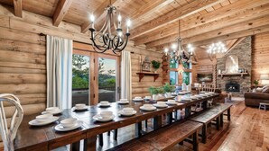 A long wooden dining table set with white plates and bowls, surrounded by benches, in a log cabin with wooden walls and a stone fireplace. - Curated, One of a kind 7,000 sqft. Lodge, VIEWS & Pool (Sevierville)