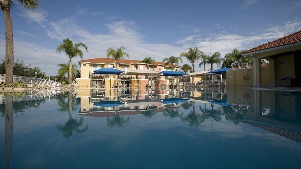 Ett hotell med en swimmingpool, palmer och en klar himmel.