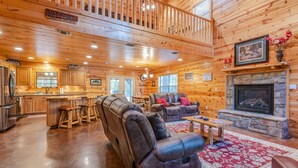 A spacious log cabin interior with a living room, a fireplace, a kitchen, and a balcony. - Relax by Broken Bow Lake, your cozy 3-bedroom Hochatown retreat (Broken Bow)