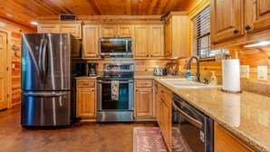 A modern kitchen with wooden cabinets, stainless steel appliances, granite countertops, and a central island. - Relax by Broken Bow Lake, your cozy 3-bedroom Hochatown retreat (Broken Bow)