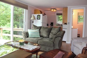 A cozy living room with a sofa, a coffee table with a vase of flowers, and a view of the kitchen in the background.