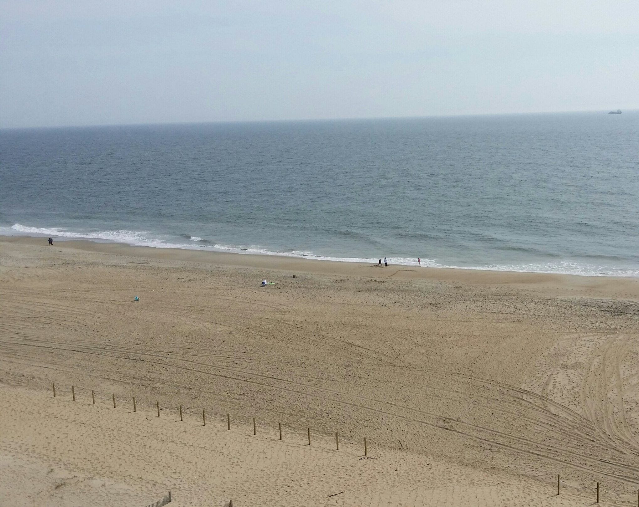 Une vaste plage de sable, avec une clôture au premier plan et une mer calme à l’arrière-plan.