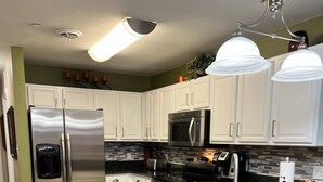 A modern kitchen with white cabinets, stainless steel appliances, a granite countertop, and black bar stools.