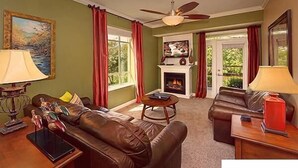 A living room with a fireplace, leather sofas, a television, and a ceiling fan.