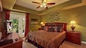 A bedroom with a large bed, two bedside tables with lamps, a ceiling fan, and a TV on a dresser.