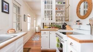 A kitchen with white cabinets, a stove, and a sink. There are bananas and vegetables on the counter.