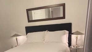 A neatly made bed with white linens, a dark headboard, and two bedside lamps. - Downtown!  Great neighborhood!  Walk everywhere downtown!   (Anchorage)