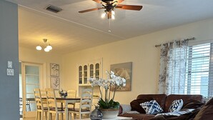 A living room with a brown leather sofa, a dining area with a white table and chairs, and a ceiling fan. - Charming Sarasota Home • Near Beaches & Downtown, 3bed, 2 bath. (Sarasota)
