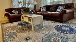 A living room with two brown leather sofas, a coffee table, a potted plant, and a patterned rug. - Charming Sarasota Home • Near Beaches & Downtown, 3bed, 2 bath. (Sarasota)