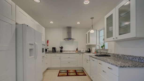 A modern kitchen with white cabinets, granite countertops, and a stainless steel range hood. - Charming Sarasota Home • Near Beaches & Downtown, 3bed, 2 bath. (Sarasota)