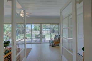 Enjoy the serene view from this sunroom, featuring a sliding door to the outdoor patio and a comfortable wicker chair.