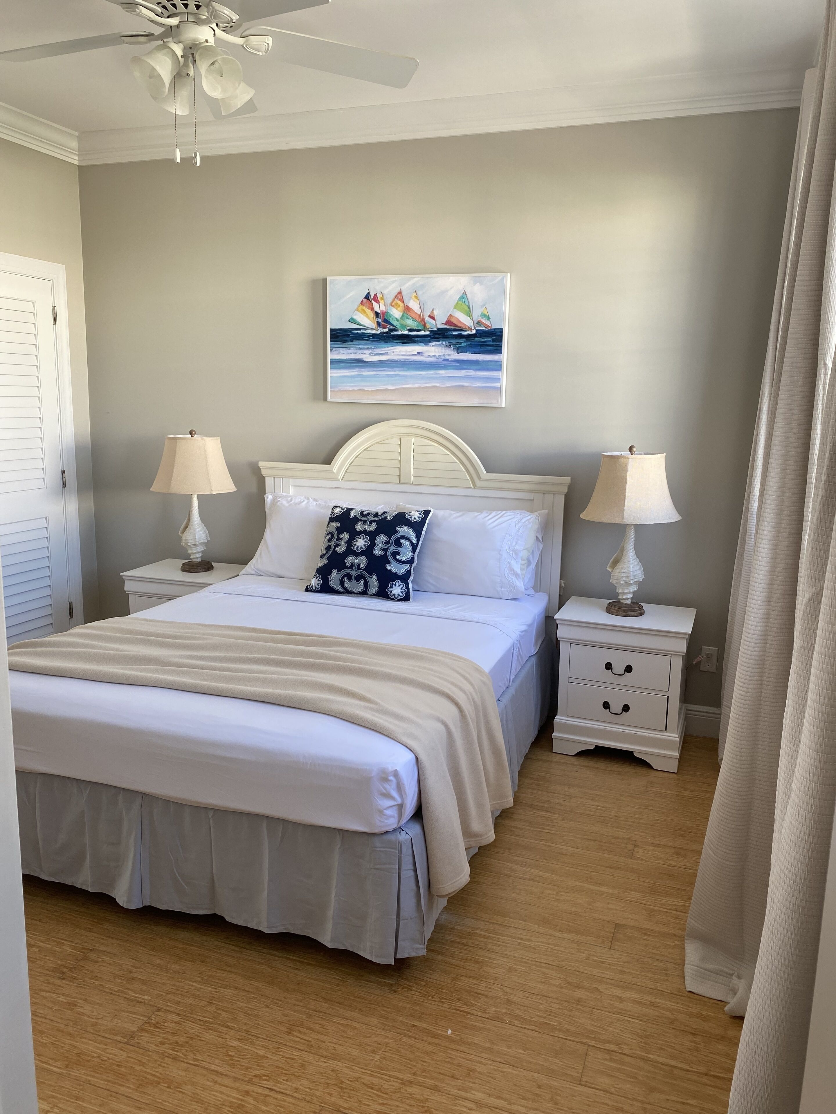Une chambre à coucher avec un lit, deux tables de chevet avec des lampes, un ventilateur de plafond et un tableau au mur.