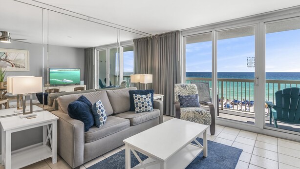 A modern hotel room with a balcony, a sofa, a TV, and a view of the beach.