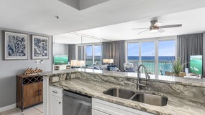 A modern kitchen with a marble countertop, stainless steel sink, and a view of the ocean.