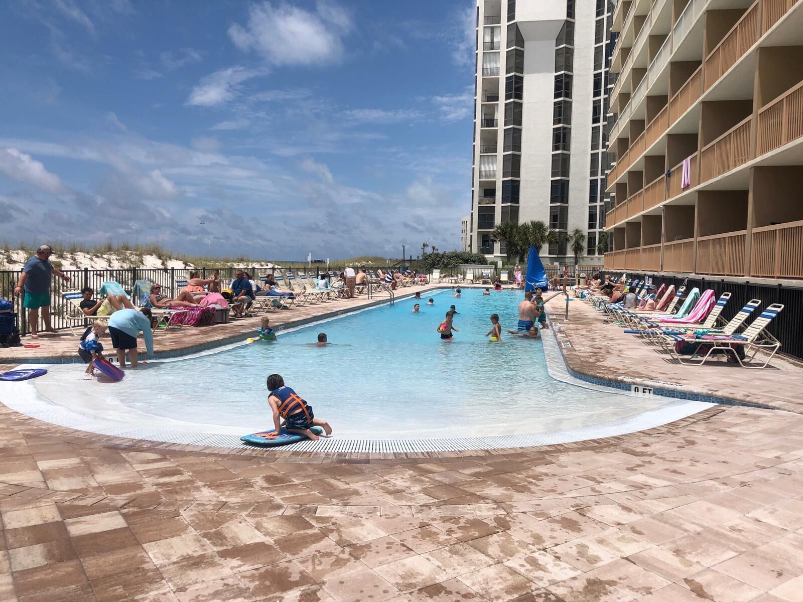 A swimming pool area with multiple pools, lounge chairs, and a high-rise building in the background.