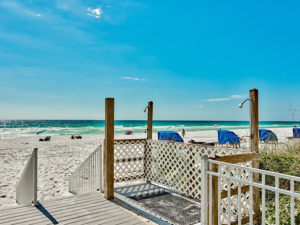 A wooden deck leading to a beach with a clear view of the ocean and beach chairs.