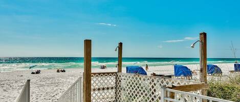 A wooden deck leading to a beach with a clear view of the ocean and beach chairs.