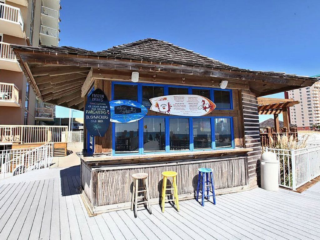 A wooden building with a signboard, three stools, and a trash can.