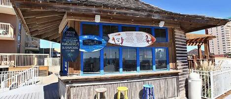 A wooden building with a signboard, three stools, and a trash can.