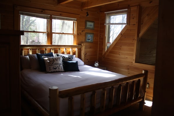 Un dormitorio de cabaña de madera con una cama, almohadas y una mesita de noche.