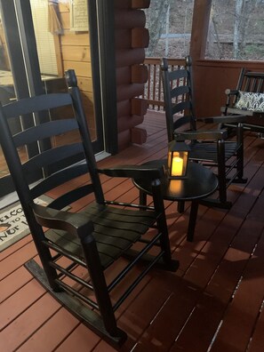 A wooden deck with black metal chairs and a table, a lit lantern, and a wooden cabin in the background. - Log cabin getaway near Gatlinburg. (Sevierville)