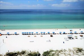 A beach with white sand, clear turquoise water, and blue umbrellas.