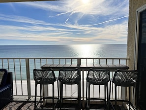 Ein Balkon mit Tisch und Stühlen mit Blick auf das Meer, an einem Tag mit blauem Himmel und deutlich sichtbaren Kondensstreifen.