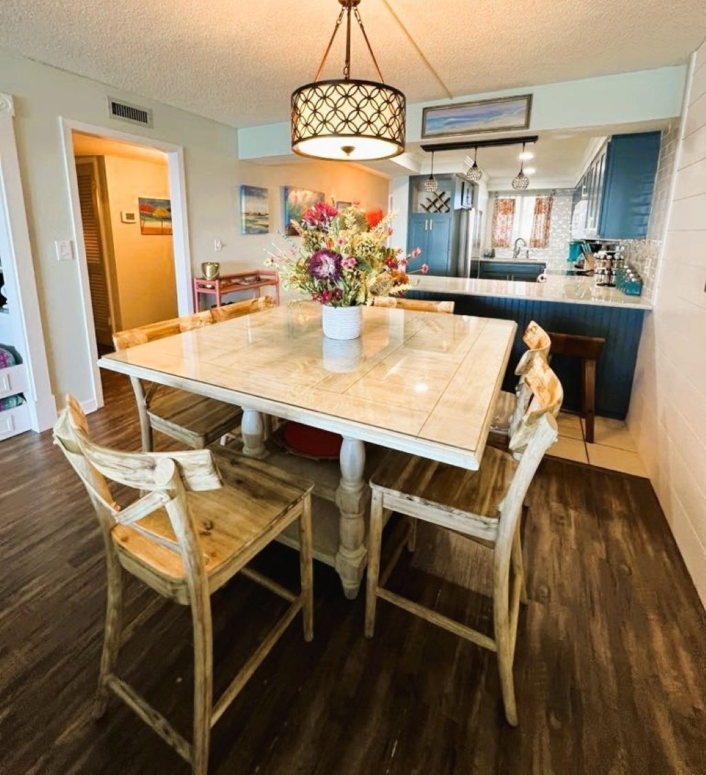 A dining area with a marble table, wooden chairs, a vase of flowers, and a hanging light fixture.
