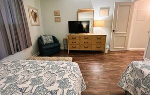A bedroom with two beds, a dresser, a TV, and a door.