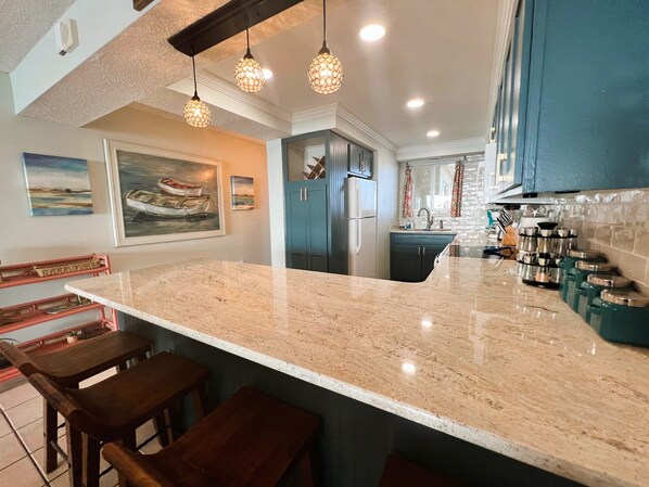 A kitchen with a marble countertop, hanging pendant lights, and a refrigerator.