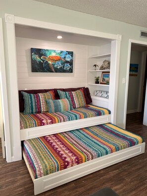 Ein Schlafsofa im Loft-Stil mit farbenfroher, gemusterter Bettdecke und Kissen, ein Gemälde einer Meeresschildkröte darüber und eine kleine Ablage mit Dekorationen.