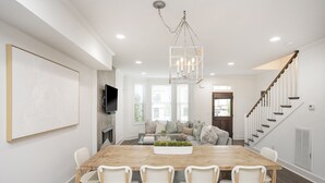 Un vaste espace dédié à la salle à manger, avec une table en bois et des chaises en osier, un lustre et un escalier menant à un autre niveau.