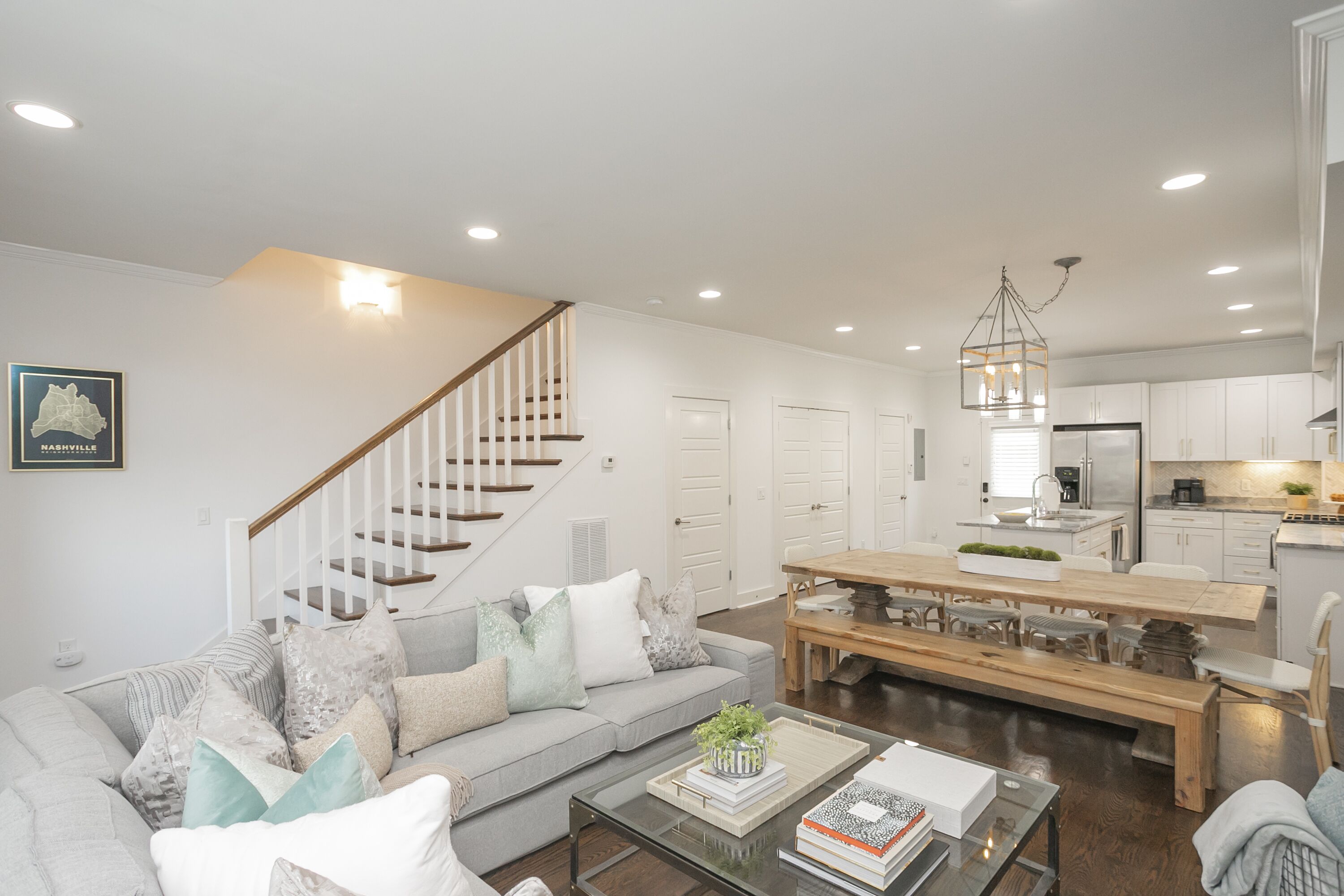A spacious living area with a sofa, coffee table, and a dining table with benches. A staircase leads to a second floor.