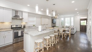 Une cuisine moderne avec des meubles blancs, un îlot central doté de tabourets, des appareils en acier inoxydable et des luminaires suspendus.