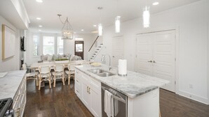 Une cuisine moderne avec des meubles blancs, un plan de travail en marbre et des luminaires suspendus.