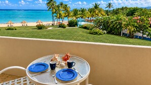 Un balcon avec une table dressée pour deux personnes, donnant sur une plage bordée de palmiers et surplombant un ciel dégagé.