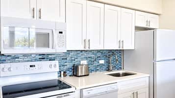 A kitchen with white cabinets, a microwave, stove, dishwasher, and a sink with a blue-tiled backsplash.