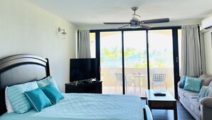 Ein Hotelzimmer mit einem Bett, einem Fernseher, einem Deckenventilator, einem Balkon mit Gartenmöbeln und einem Sofa.