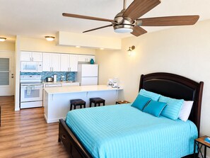 Ein Schlafzimmer mit Bett, Deckenventilator, einer Küchenzeile und einem Badezimmer.