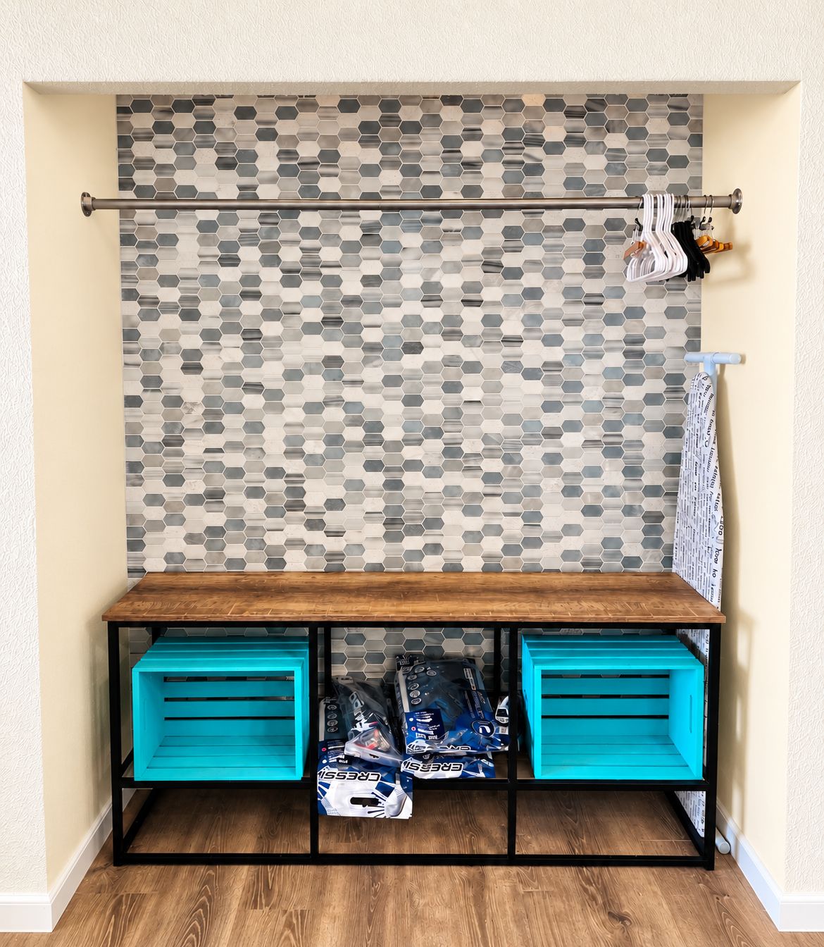 A room with a wooden bench, a metal rack with bags, and a patterned wall.