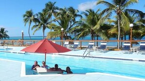 Ein Poolbereich mit Liegestühlen und Sonnenschirmen, Palmen und Blick aufs Meer.