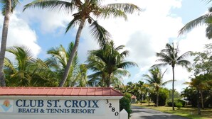 Schild für das Club St. Croix Beach & Tennis Resort, mit rotem Dach und weißen Wänden, umgeben von Palmen und blauem Himmel.