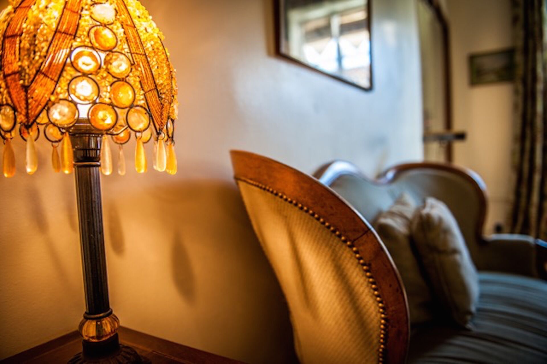 A lamp with a patterned shade and a wooden table beside a bed with a headboard and pillows.