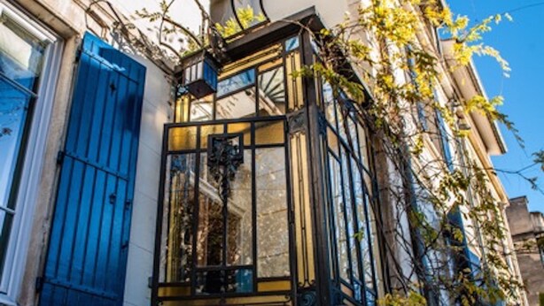 Ein Eckgebäude mit Treppe, einem Fenster mit blauen Rollläden und einem Balkon mit schmiedeeisernem Geländer.